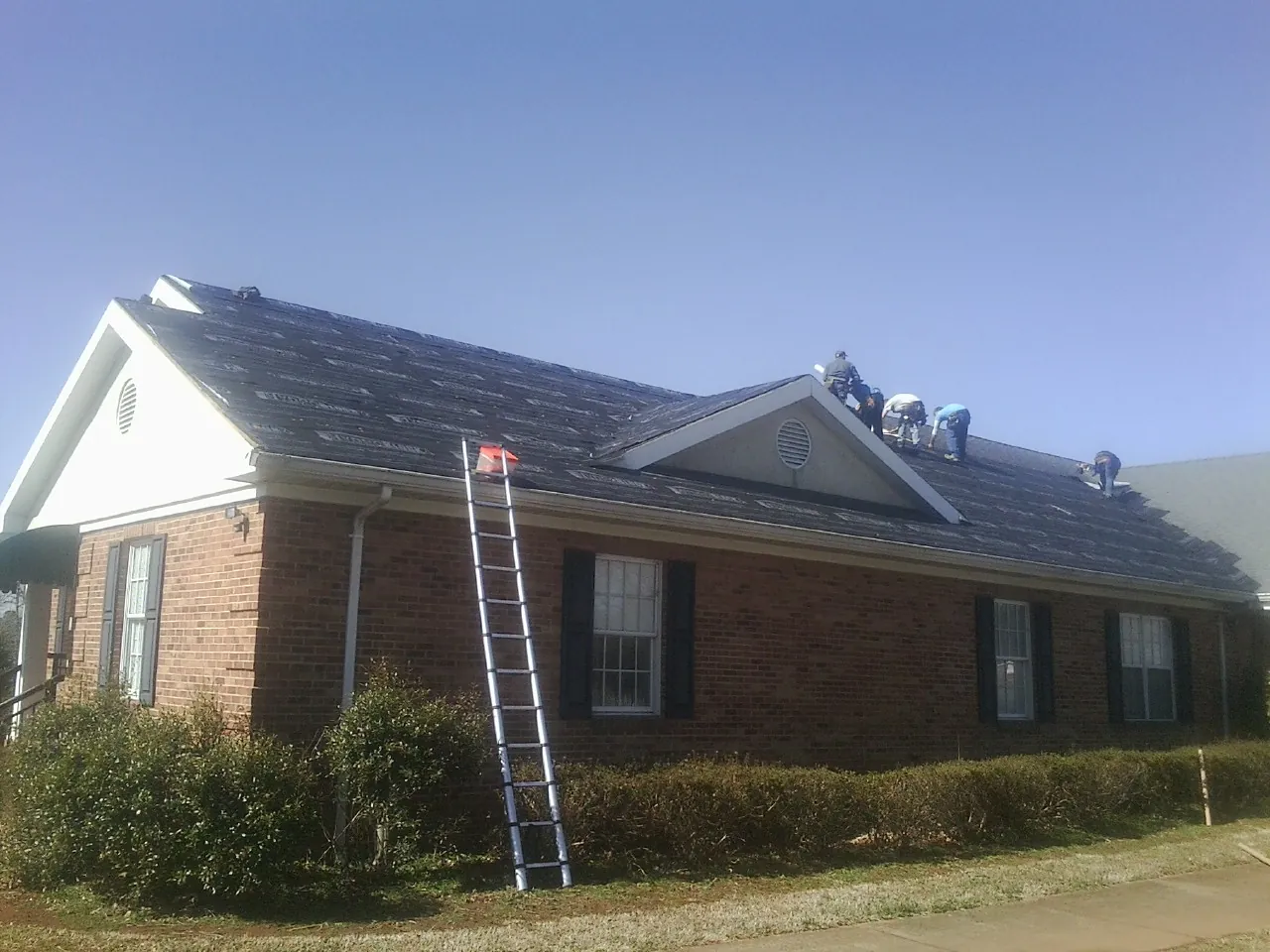 Crew tearing shingles off a brick ranch roof with a ladder set — Emergency Roof Repair work by our crew in Monponsett