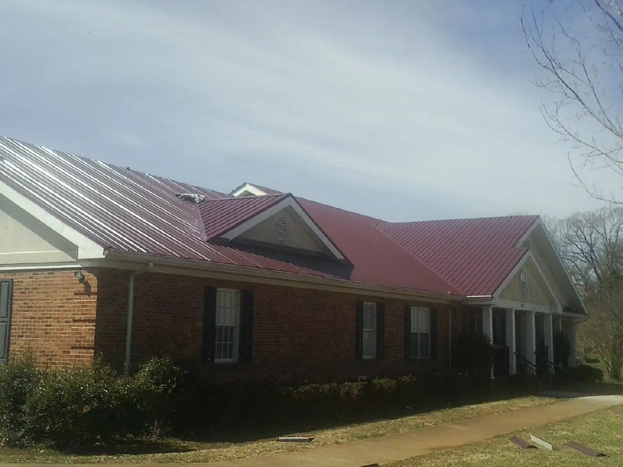 Red metal roof with gabled entries on a long brick building, from a Hail Damage Roof Repair job in Monponsett