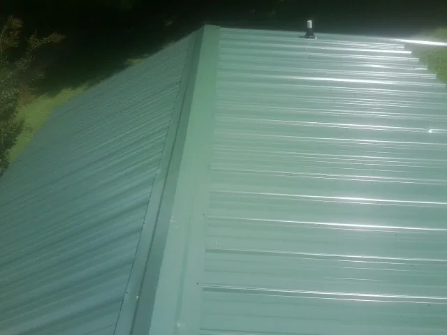 New green metal panels meeting at the ridge of a roof — Flat Roof Repair work by our crew in Monponsett