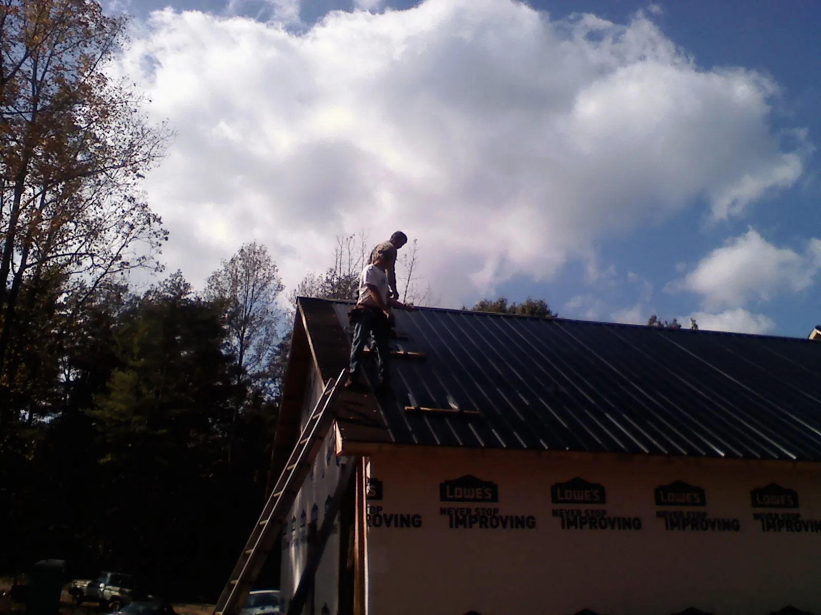 Roofer fastening dark metal panels high against a cloudy sky, from a Roof Inspection job in Monponsett