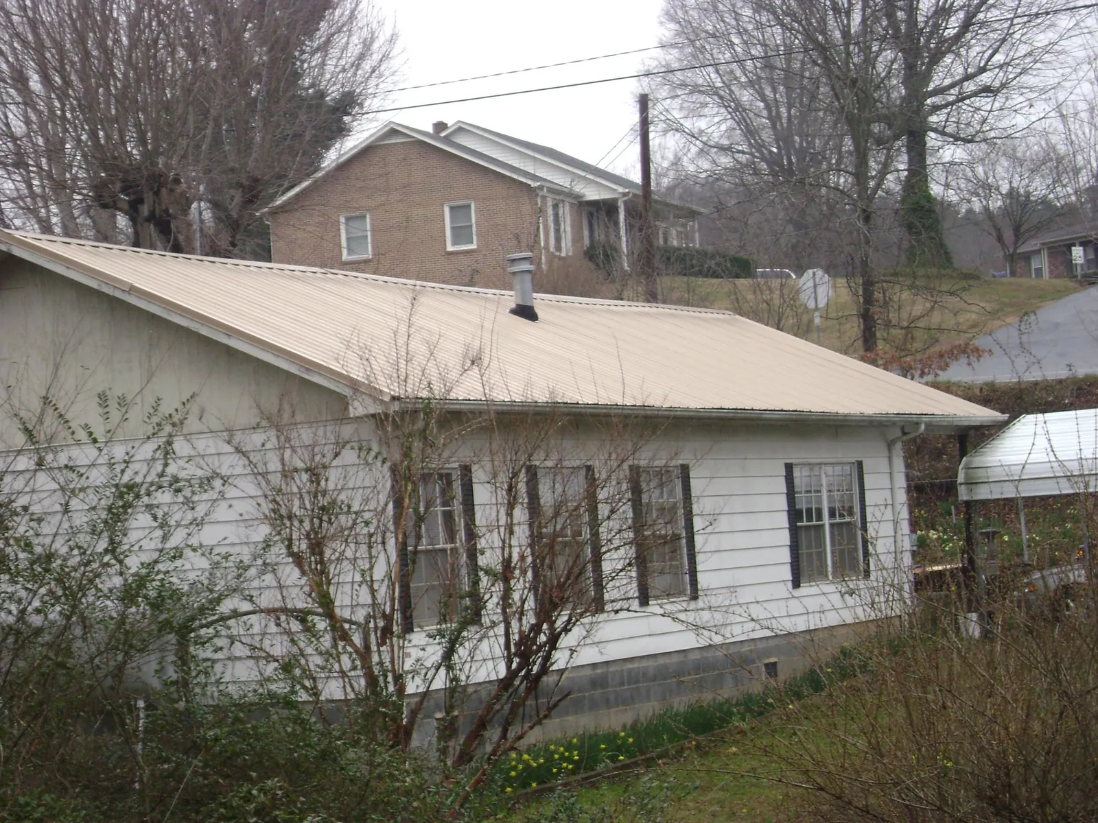 Tan metal roof on a white sided house set into a hillside — Commercial Roofing by Roofing Brothers in Monponsett